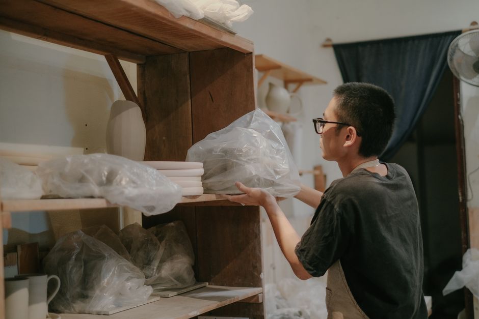 A focused artisan arranges handcrafted pottery on studio shelves.